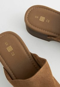 Bruine suède wedge sandalen met een slank ontwerp, afgeronde neuzen en zichtbare stiksels. Gemarkeerd met maat en merklogo in het goud.