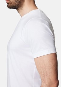 Biała bawełniana koszulka z krótkim rękawem. Okrągły dekolt i dopasowany krój. Gładka tekstura, bez widocznych wzorów ani grafik. Pokazany widok z boku.