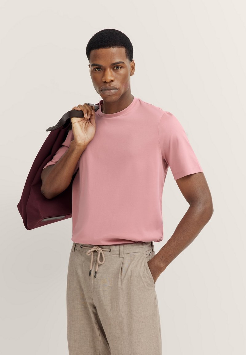 Pink short-sleeve t-shirt made of smooth fabric, paired with light beige trousers featuring a drawstring waist and pockets, holding a maroon jacket.
