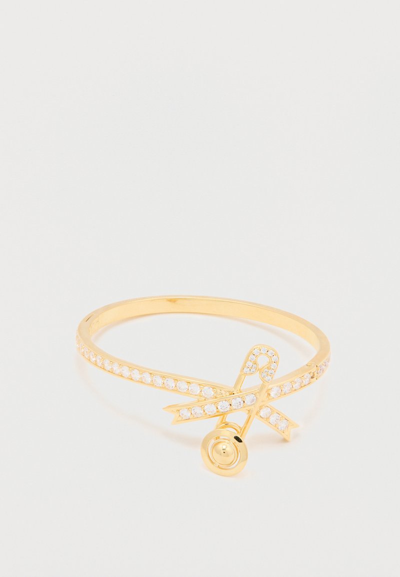 Arany tónusú gyűrű vékony pánttal, kristálydíszítéssel és dekoratív szalag mintával, kerek részlettel.