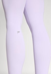 Light purple leggings with a smooth texture, featuring a silver logo near the ankle and a fitted design that contours to the legs.