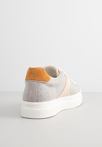Sneaker grigio e beige con upper in feltro testurizzato, accentuazione arancione in suede sul tallone e suola bianca con un motivo a diamante.