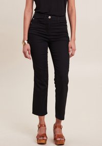 Jean en denim noir taille haute avec une coupe droite, doté de poches avant et d'un détail de bouton argenté. Associé avec des sandales à plateforme marron.