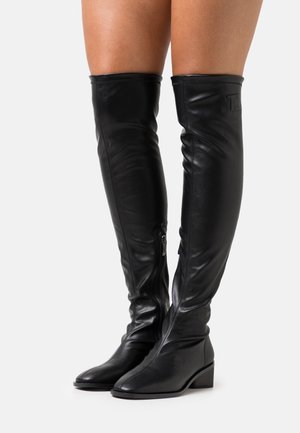 Botas de cuero negras por encima de la rodilla con un diseño elegante, cierre de cremallera en el lateral y un tacón bajo y ancho para mayor estabilidad. Textura suave.