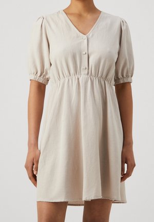 Beige korte mouwen jurk met V-hals, drie knopen aan de voorkant, elastische taille en geplooide mouwen met een lengte tot boven de knieën, gedragen door een staand persoon.