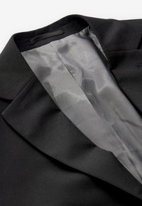 Fekete blézer sima külső anyaggal és világosszürke hálós béléssel a gallér és a hajtóka területén.