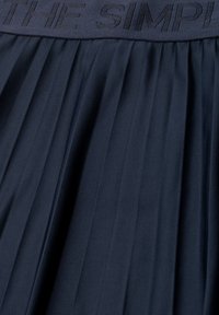 Dark pleated fabric with an elastic waistband featuring subtle raised text reading "THE SIMPLI".
