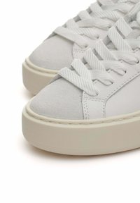 Zapatillas blancas que presentan una combinación de cuero liso y suave gamuza, puntera redonda, cordones blancos en contraste y una suela de goma gruesa.