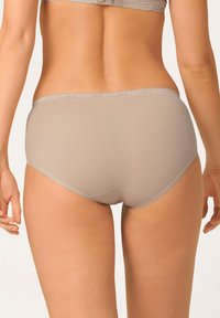 Slip in cotone beige con vita bassa, texture liscia e design semplice. Presenta un taglio semplice e cuciture discrete lungo i bordi.