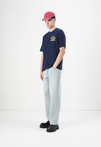 Navy blue cotton t-shirt with yellow graphic, light blue denim jeans, and black chunky footwear. Red cap with black accents.