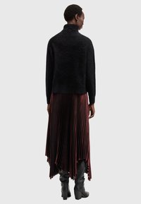 Maglione nero peloso con colletto alto e maniche lunghe indossato sopra una gonna plissettata bordeaux. Stivali neri con tacco completano l'outfit.