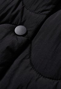 Czarna tkanina pikowana o gładkiej fakturze, z okrągłym czarnym guzikiem i zaokrąglonym pikowaniem, podkreślająca miękki, wyściełany design.