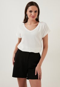 Top bianco a maniche corte con scollatura a V e motivo testurizzato, abbinato a pantaloni corti neri a vita alta. Design semplice e colori neutri.