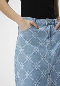 Vaaleansinisestä denimmekosta, jossa on timanttikuvio ja kukkakoristeet. Siinä on etutaskut ja etupainon sulkeminen.