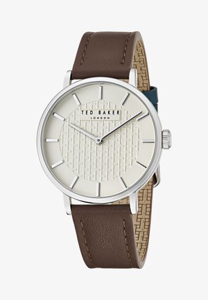 Reloj con correa de cuero marrón y una esfera crema texturada, acentos plateados y una caja redonda de acero inoxidable. Presenta un patrón tejido en el centro.