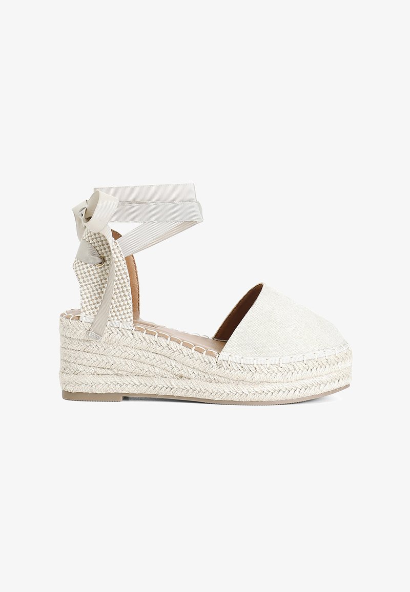 Beige espadrilové sandály na klínu s textilním svrškem, pletenou juty podešví a stužkami na kotníky. Kulatá špička a polstrovaná stélka.