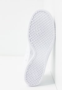 Semelle blanche de basket avec des motifs de traction circulaires et en forme de losange affichée sur fond blanc.