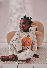 Børnepyjamas i cremefarve med mønstre af græskar og spøgelser. Blød bomuld, rund halsudskæring og elastiske manchetter. Bemærkelsesværdig blød græskardetalje.