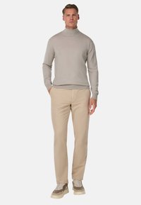 Pullover a collo alto grigio chiaro abbinato a pantaloni beige e sneakers grigie e crema. Design semplice con silhouette aderente e colori neutri.