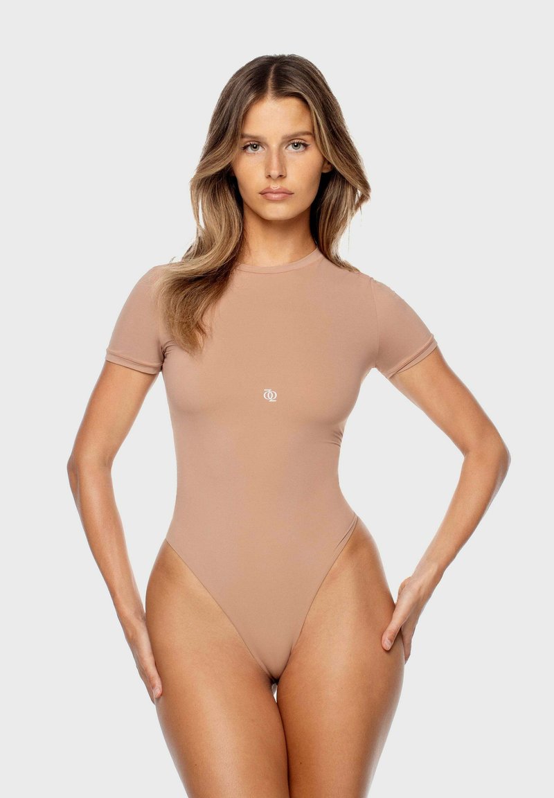 Bodysuit nude à manches courtes avec une jambe haute, fabriqué en tissu lisse. Présente un petit logo blanc à l'avant. Design simple et ajusté.