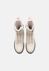 Botas beige de cuero con cordones, forro de borreguito, punta redonda y cremalleras laterales. Cuenta con una suela negra con detalles texturizados.