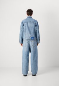 Light blue denim jacket and wide-leg jeans with a blue brand tag on the back. Features a classic collar and visible stitching details.