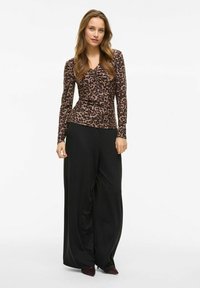 Dlouhý rukáv top v tygrovaném vzoru s výstřihem do V, kombinovaný s širokými černými kalhotami. Outfit má hladké textury a přiléhavý siluetu.