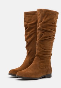 Bottes montantes en daim marron avec texture froncée, bout arrondi et semelle plate. Présentent une finition lisse et des détails discrets de couture.
