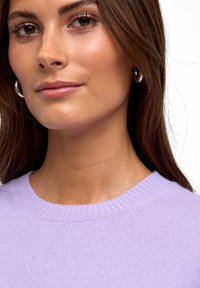 Maglione lilla con scollatura a girocollo a costine, caratterizzato da una fine trama a maglia. Il modello ha capelli castani di lunghezza media e indossa orecchini a cerchio in argento.