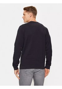 Felpa nera a maniche lunghe con colletto a girocollo. Tessuto morbido con polsini e orlo a coste. Indossata con jeans grigi, presenta un design semplice e moderno.