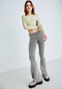 Off-shoulder, lysegul ribbestrikket topp med lange ermer; ribbet, flagrende, grå og svartstripete strikkede bukser med sidespenner.