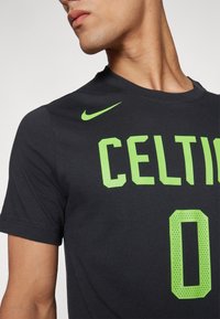 Must have lühikeste varrukatega must Nike t-särk, mis on varustatud suure rohelise "CELTIC" tekstiga ning punktmustritega numbri "0". T-särgil on ümar kaelus ja liibuvad varrukad.