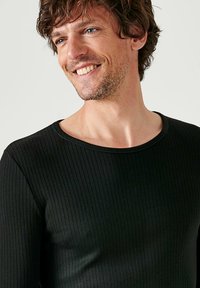 Zwarte ribgebreide langemanig shirt met een ronde halslijn. Zachte textuur, slim fit ontwerp en contrasterend detail bij de halslijn.