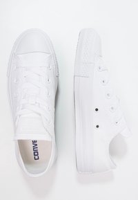 Ein Paar weiße Low-Top Converse-Sneaker, einer von oben und der andere von der Seite gezeigt, auf einem weißen Hintergrund.