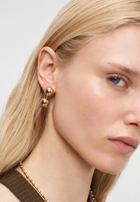 Goldohrringe mit zwei kugelförmigen Formen, eine über der anderen, mit einer glatten, glänzenden Oberfläche und einem kleinen Verbindungsteil.