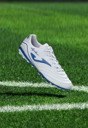 Chaussure de football blanche et bleue en l'air au-dessus d'un terrain en herbe près des lignes de délimitation blanches.