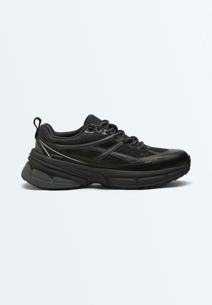 Baskets noires basses de sport avec tige en mesh et synthétique, semelle épaisse et rembourrée, fermeture à lacets et languette au talon.