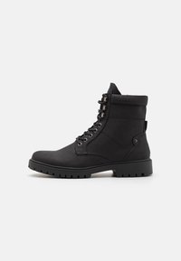 Botines negros con un upper de tela texturizada, cordones en la parte delantera, cuello acolchado y suela de goma resistente con un leve tacón y detalle lateral.