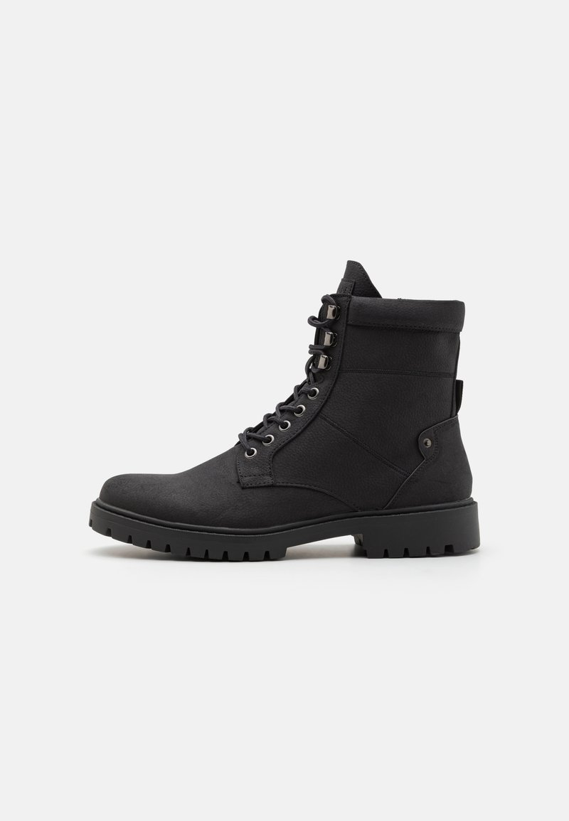 Botines negros con un upper de tela texturizada, cordones en la parte delantera, cuello acolchado y suela de goma resistente con un leve tacón y detalle lateral.