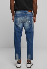 Jeans de denim azul con un acabado deslavado, detalles desgastados y corte recto. Presenta bolsillos traseros y dobladillos deshilachados.