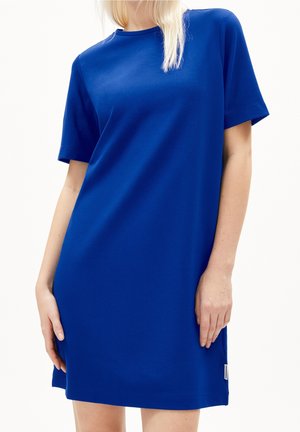 Kobieta ubrana w prostą, krótkim rękawem, do kolan sukienkę w kolorze królewskiego błękitu z okrągłym dekoltem na białym tle.