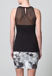 Schwarzes ärmelloses Oberteil mit transparentem Rücken, kombiniert mit einem enganliegenden grauen und schwarzen Batik-Rock. Glatte Textur durchgehend.