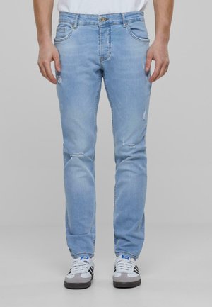 Light blue denim jeans with a slim fit, featuring distressing on the knees, five pockets, and a metal button fastening.