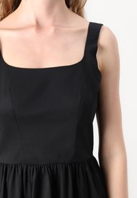 Μαύρο φόρεμα με τετράγωνη λαιμόκοψη, φαρδιά μανίκια και συγκεντρωμένη, υφασμάτινη φούστα. Λείος ύφασμα χωρίς ορατά σχέδια.