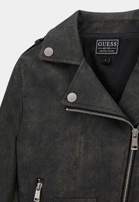 Chaqueta de cuero sintético negra con herrajes plateados, cierre de cremallera y cuello clásico. Acabado texturizado con un aspecto ligeramente desgastado.