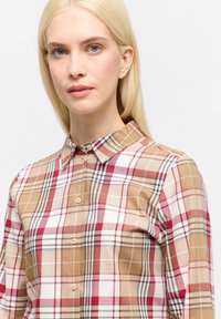 Checkered shirt featuring a blend of beige, red, and white, with a collar, button front, and long sleeves. Soft fabric with a smooth texture.