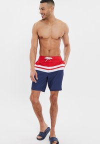 I pantaloni da bagno rossi e blu navy presentano strisce bianche orizzontali, una vita elasticizzata con cordino, un tessuto leggero e tasche laterali.