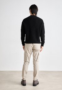 Suéter negro de punto, pantalones cargo beige con bolsillos laterales, calzado gris. Diseño simple con puños y cintura acanalados, colores neutros.