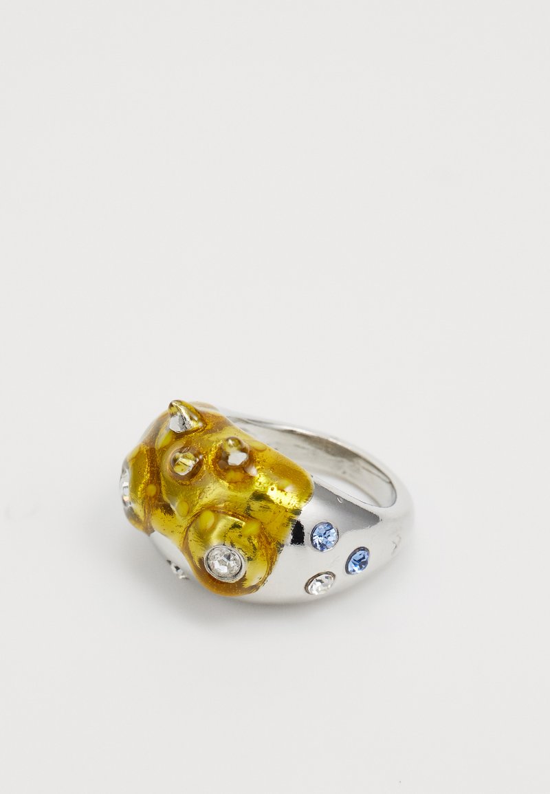 Sidabrinis žiedas, turintis nelygų geltoną raštą su burbulais ir keliais brangakmeniais, įskaitant mėlynas ir skaidrias akcentus, vienoje pusėje.