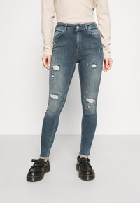 Vaqueros skinny de mezclilla en un tono azul desgastado con detalles destruidos, que cuentan con bolsillos frontales, cierre de botón y un diseño ajustado.